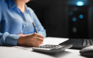 Image showing woman with calculator and papers at night office