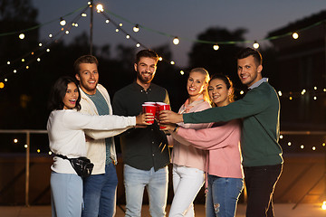 Image showing friends clinking party cups on rooftop at night