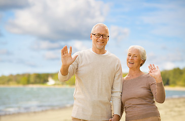 Image showing happy senior couple waving hands on beach