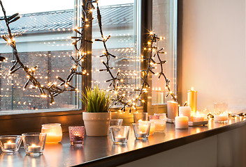 Image showing candles burning on window sill with garland lights