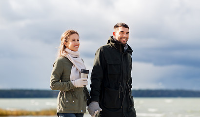 Image showing couple with tumbler walking along autumn beach