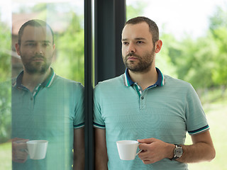 Image showing young man drinking morning coffee by the window