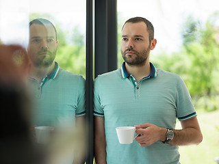 Image showing young man drinking morning coffee by the window