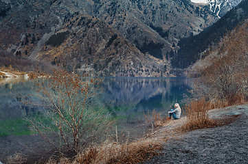 Image showing Woman listening music at the water's edge of mountain lake