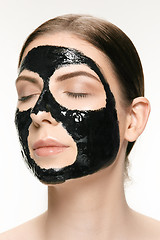 Image showing Young beautiful woman applying a mask for the face of the therapeutic black mud. Spa treatment