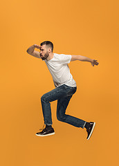 Image showing Freedom in moving. handsome young man jumping against orange background