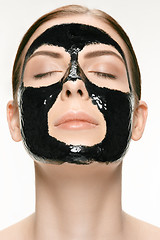 Image showing Young beautiful woman applying a mask for the face of the therapeutic black mud. Spa treatment