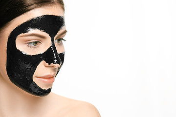 Image showing Young beautiful woman applying a mask for the face of the therapeutic black mud. Spa treatment