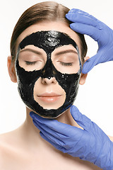 Image showing Young beautiful woman applying a mask for the face of the therapeutic black mud. Spa treatment