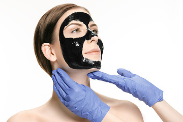 Image showing Young beautiful woman applying a mask for the face of the therapeutic black mud. Spa treatment