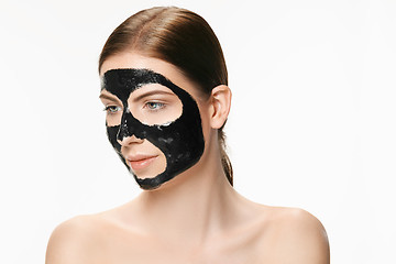 Image showing Young beautiful woman applying a mask for the face of the therapeutic black mud. Spa treatment