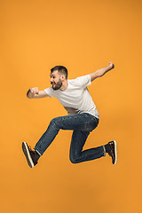 Image showing Freedom in moving. handsome young man jumping against orange background