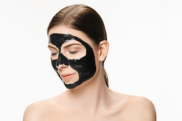 Image showing Young beautiful woman applying a mask for the face of the therapeutic black mud. Spa treatment
