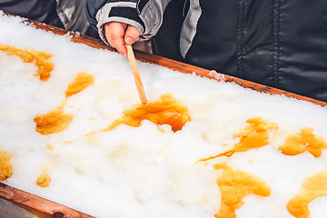 Image showing Child putting maple taffy on a wooden stick 