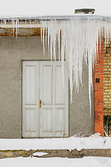 Image showing Huge icicles hang from the roof of an abandoned house with wooden door