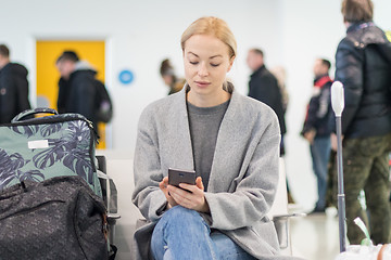 Image showing Female traveler using her cell phone while waiting to board a plane at departure gates at airport terminal.