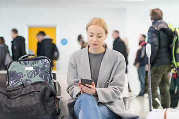 Image showing Female traveler using her cell phone while waiting to board a plane at departure gates at airport terminal.