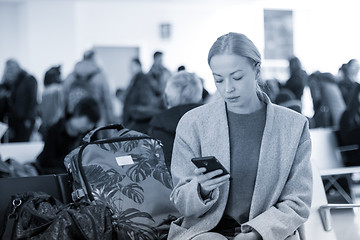 Image showing Female traveler reading on her cell phone while waiting to board a plane at departure gates at airport terminal.