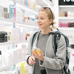 Image showing Blond young female traveler wearing travel backpack choosing perfume in airport duty free store.