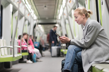 Image showing Beautiful blonde woman wearing winter coat reading on the phone while traveling by metro public transport.