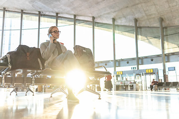 Image showing Female traveler talking on her cell phone while waiting to board a plane at departure gates at airport terminal.