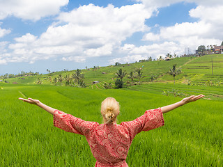 Image showing Relaxed fashionable caucasian woman wearing red asian style kimono, arms rised to sky, enjoying pure nature of beautiful green rice fields on Bali.