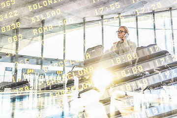 Image showing Female traveler talking on her cell phone while waiting to board a plane at departure gates at airport terminal.