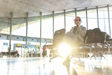 Image showing Female traveler talking on her cell phone while waiting to board a plane at departure gates at airport terminal.