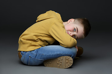 Image showing Handsome little boy in jeans sitting on floor