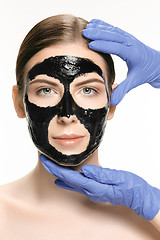 Image showing Young beautiful woman applying a mask for the face of the therapeutic black mud. Spa treatment