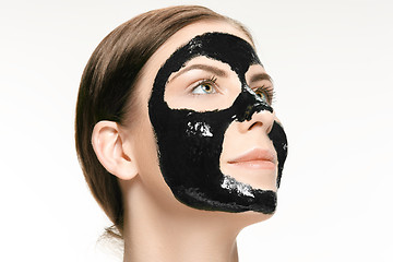 Image showing Young beautiful woman applying a mask for the face of the therapeutic black mud. Spa treatment