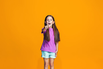 Image showing The happy teen girl pointing to you, half length closeup portrait on orange background.