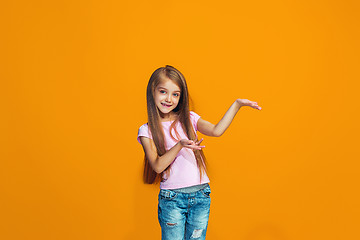 Image showing The happy teen girl presenting something, half length closeup portrait on orange background.