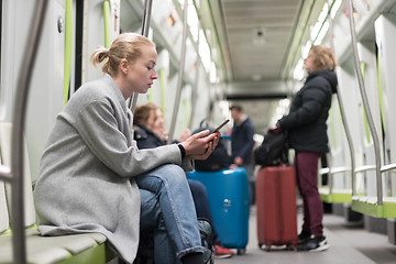 Image showing Beautiful blonde woman wearing winter coat reading on the phone while traveling by metro public transport.