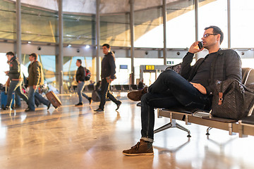 Image showing Male traveler talking on his cell phone while waiting to board a plane at departure gates at airport terminal.