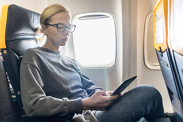 Image showing Woman wearing glasses reading on digital e-reader while traveling by airplane.