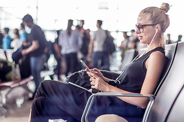 Image showing Female traveler using her cell phone while waiting to board a plane at departure gates at asian airport terminal.