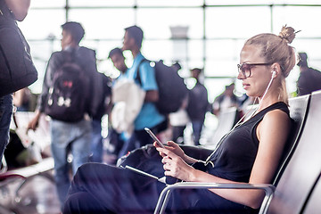 Image showing Female traveler using her cell phone while waiting to board a plane at departure gates at asian airport terminal.