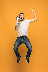 Image showing Jumping fan on orange background. The young man as soccer football fan with megaphone