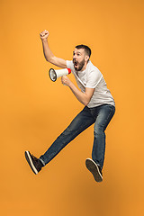 Image showing Jumping fan on orange background. The young man as soccer football fan with megaphone