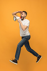 Image showing Jumping fan on orange background. The young man as soccer football fan with megaphone