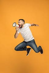 Image showing Jumping fan on orange background. The young man as soccer football fan with megaphone