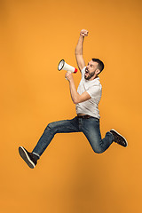 Image showing Jumping fan on orange background. The young man as soccer football fan with megaphone