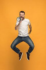 Image showing Jumping fan on orange background. The young man as soccer football fan with megaphone