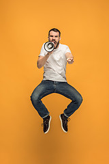 Image showing Jumping fan on orange background. The young man as soccer football fan with megaphone