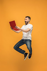 Image showing Image of young man over orange background using laptop computer while jumping.