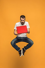 Image showing Image of young man over orange background using laptop computer while jumping.