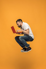 Image showing Image of young man over orange background using laptop computer while jumping.