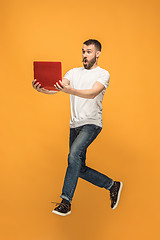 Image showing Image of young man over orange background using laptop computer while jumping.