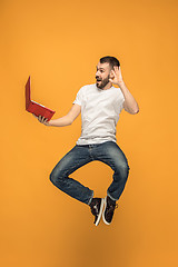 Image showing Image of young man over orange background using laptop computer while jumping.